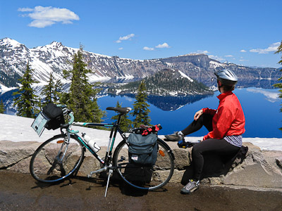 Bicycle in view of Wizard Island in the deep blue lake at Crater Lake National Park in early June when Rim Drive is closed to cars to allow snow plowing, Oregon, USA.
